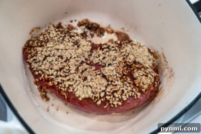 A roast piece of meat in a pot, topped with a mix of spices, herbs, and caramelized onions, ready to be cooked.