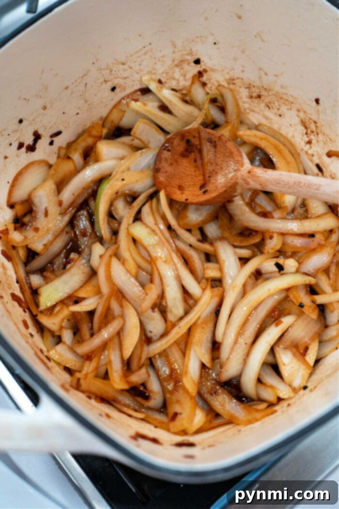 Sliced onions roasting in a pot, seasoned to perfection and stirred with a wooden spoon.