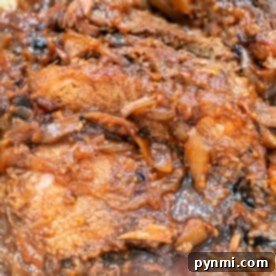 A close-up of braised beef brisket with caramelized onions in a rich, savory roast sauce.