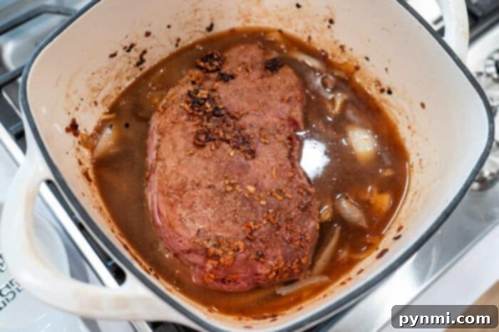 Savory roast beef simmered gently in a pot with caramelized onions and hearty broth on the stove.