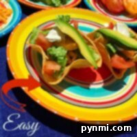 Colorful taco salad bowls filled with avocado, lettuce, and tomato slices sit on vibrant plates.
