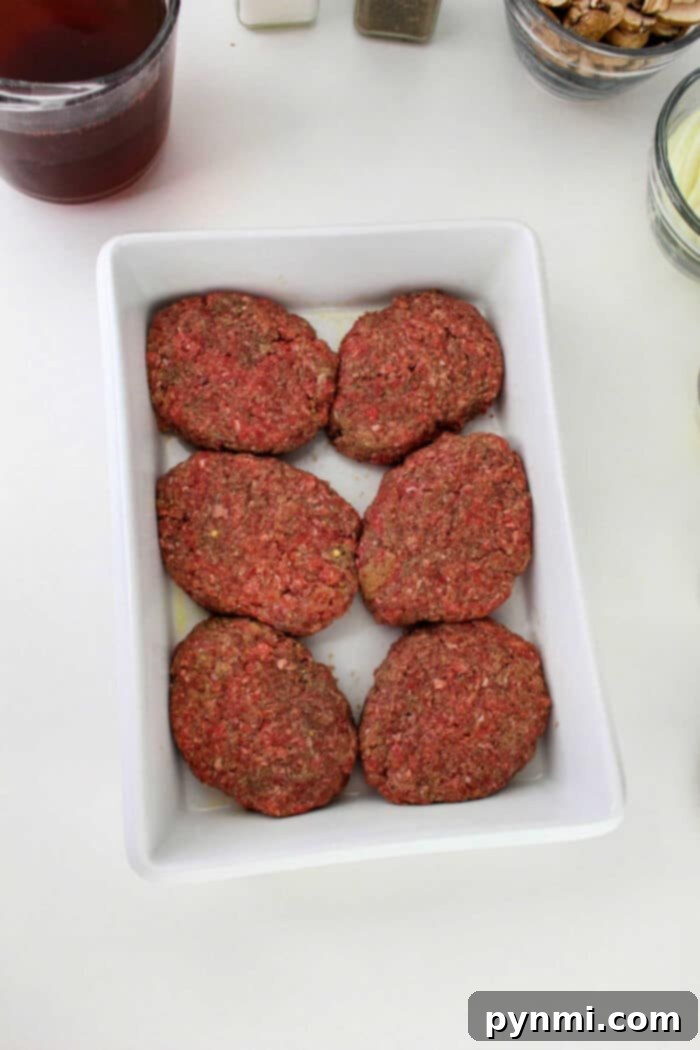 Homestyle Ground Beef Steak 5 Six raw ground beef patties, perfect for making Hamburger Steak, are arranged in a white rectangular dish on a white surface.