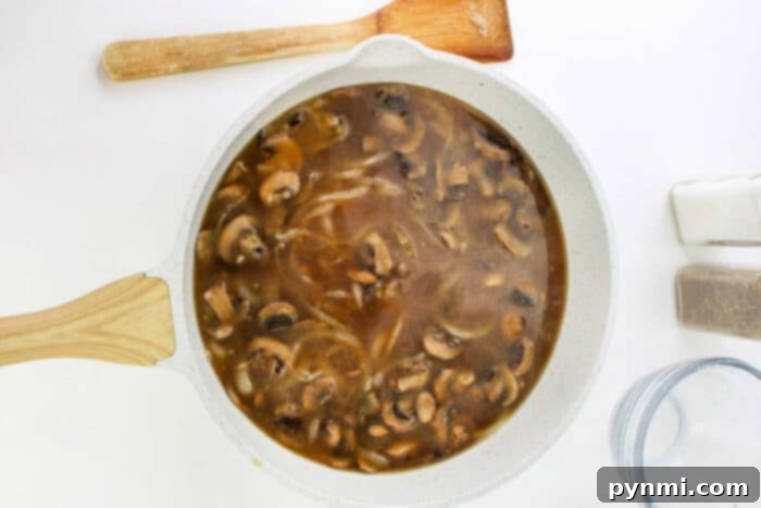 Homestyle Ground Beef Steak 6 A white skillet filled with savory mushroom and onion gravy for Hamburger Steak, next to a wooden spatula, salt, and pepper shakers.