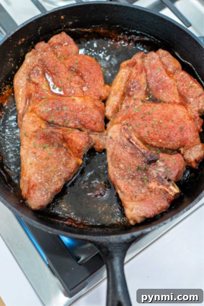 Two perfectly seasoned pork shoulder steaks beginning to sizzle and sear in a hot black cast iron skillet on a gas stovetop.