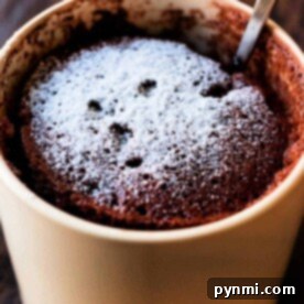 A delightful chocolate mug cake made with cake mix and a hint of mayonnaise for extra moisture, topped with powdered sugar in a beige mug, complete with a spoon inside.