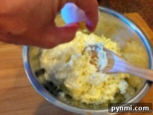 A hand cracks an egg into a metal bowl containing a mixture of shredded cheese and cream, with a wooden spoon in the bowl, preparing the filling for an easy crockpot lasagna recipe.