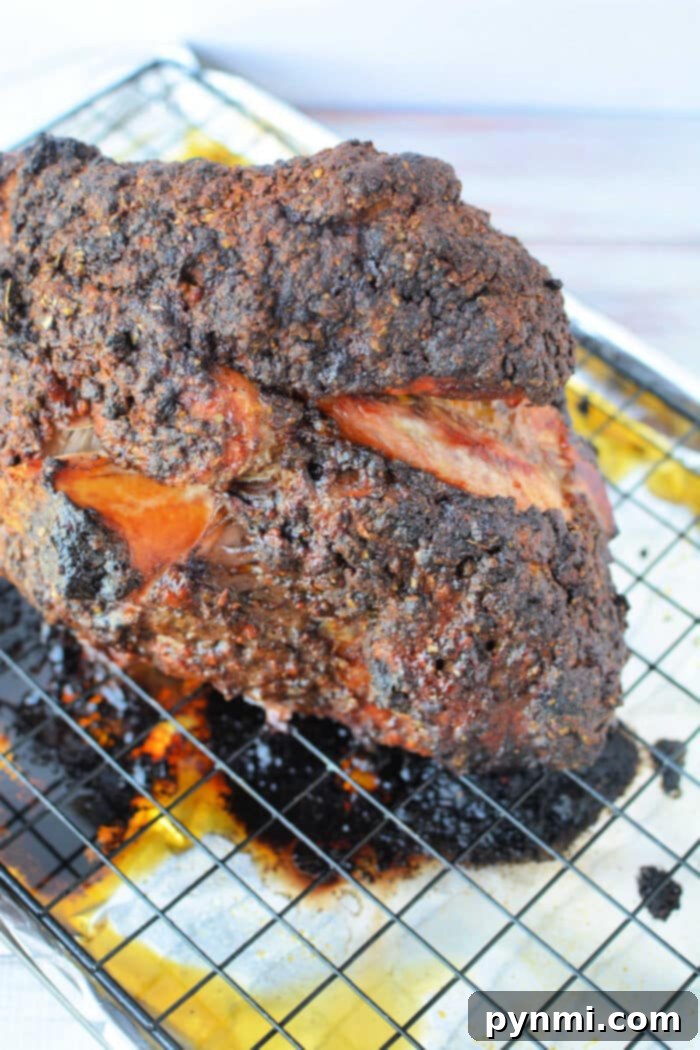 A large, crispy, blackened Pork Roast in Oven rests on a wire rack over a baking sheet with savory drippings.