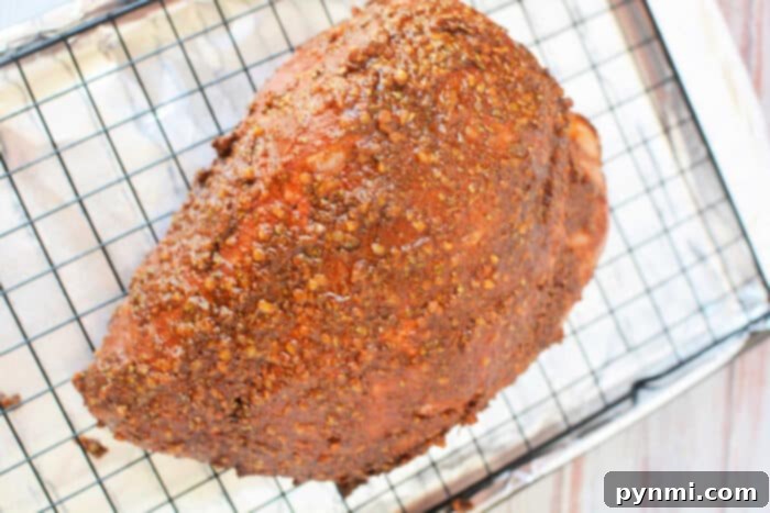 Seasoned ham on a wire rack over a foil-lined baking sheet, prepared just like a classic pork roast recipe, ready for the oven.