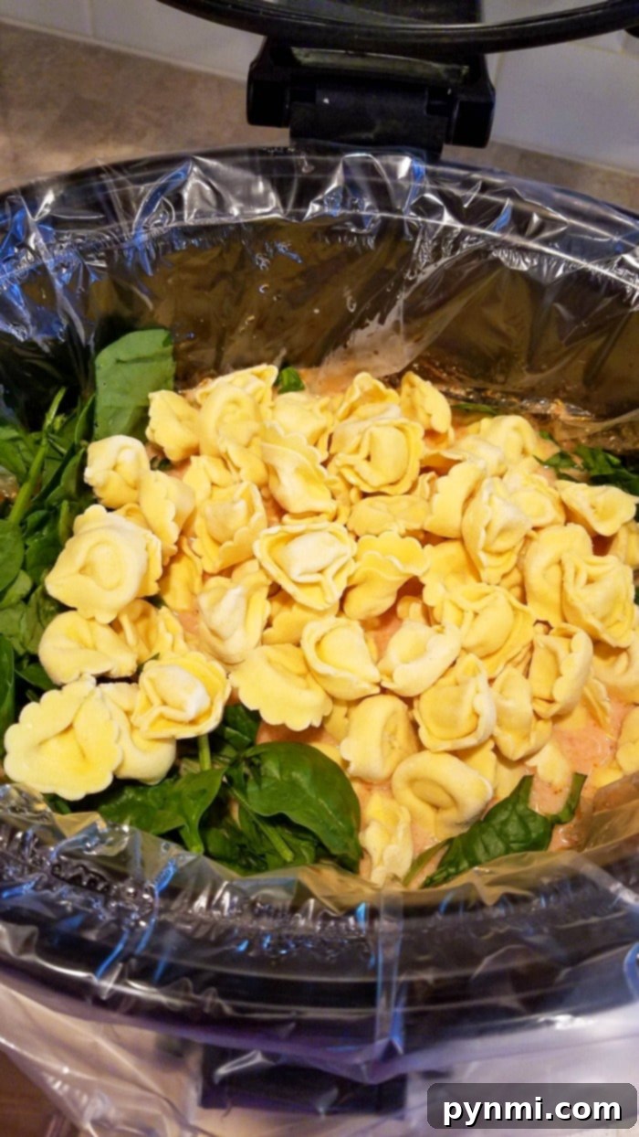 Creamy tortellini soup with spinach and tomatoes in a slow cooker, ready to be served.