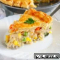 A slice of golden-crusted chicken pot pie, made from a simple recipe, sits invitingly on a white plate, brimming with vegetables.