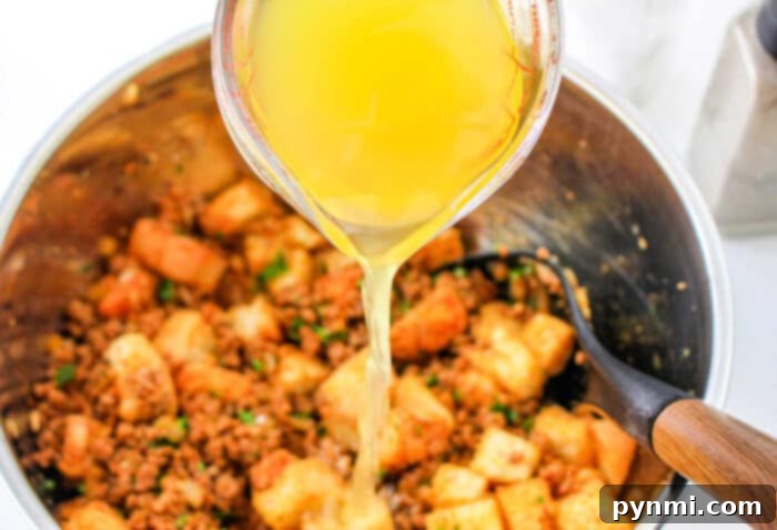Robust Chorizo Stuffing 4 A measuring cup pours broth into a bowl of stuffing mix with bread cubes, sausage, and chorizo for a flavorful chorizo stuffing.