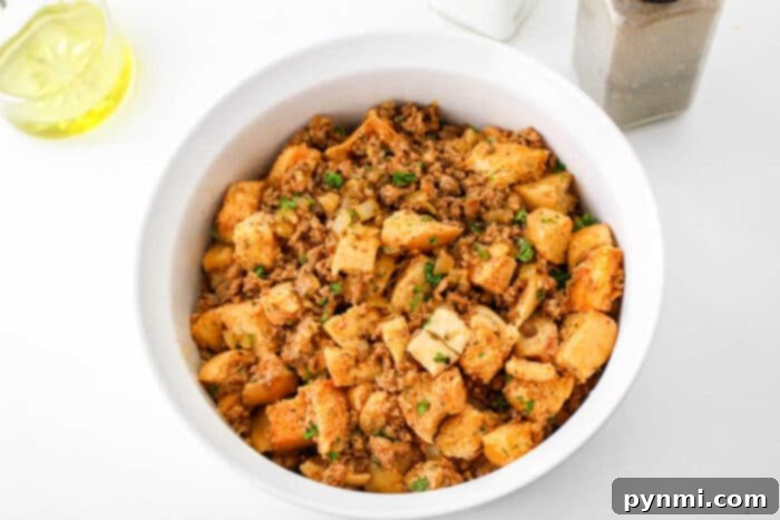 Robust Chorizo Stuffing 5 A bowl of homemade chorizo stuffing with bread cubes, herbs, and ground meat sits on a white surface.