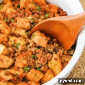 A wooden spoon in a bowl of savory chorizo stuffing, mixed with herbs and sausage.
