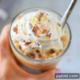 Hand holding a pumpkin spice frappuccino topped with whipped cream and chocolate shavings, with a metal straw.