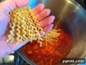 A hand gracefully holds uncooked wavy pasta over a pot of vibrant orange-hued liquid simmering on the stove, perfect for creating a delicious one-pot spaghetti masterpiece.