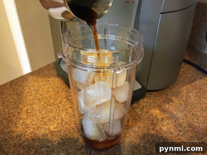 A person blending ice, coffee, and creamer in a personal blender, showcasing the ease of making a homemade frappuccino.