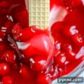 A wafer being dipped into a vibrant cherry cheesecake dip in a glass bowl.