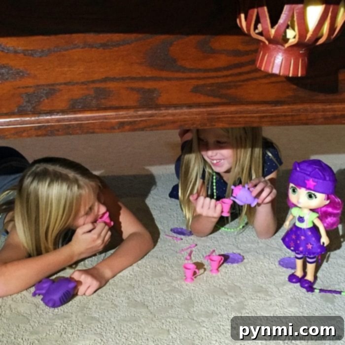 Two young girls engaged in imaginative tea party play with a Little Charmers doll and other toys