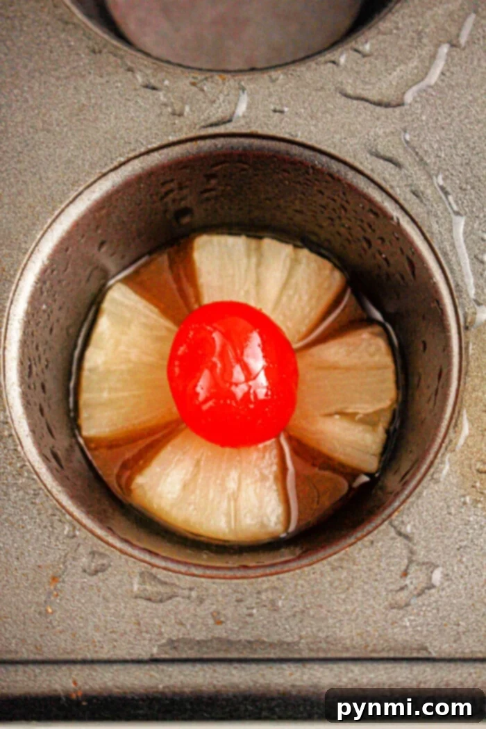 Effortless Golden Pineapple Upside Down Cupcakes 5 Four individual pineapple upside-down cupcakes in a muffin tin, each with a caramelized pineapple ring and cherry on top, ready to be flipped.