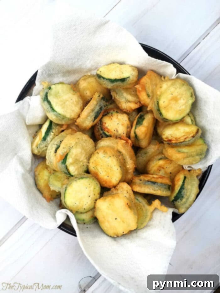 Crispy Salt and Pepper Zucchini Chips with a light tempura batter. A perfect vegetable side dish or snack that even kids will love. A bowl of crispy salt and pepper zucchini chips rests on a paper towel-lined plate, ready to be served.