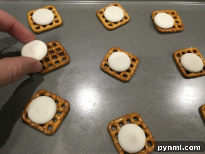 Close-up of square pretzels with white candy melts placed on top, ready for baking.