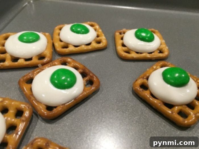A baking sheet filled with partially melted white candy melts on pretzels, fresh out of the oven.