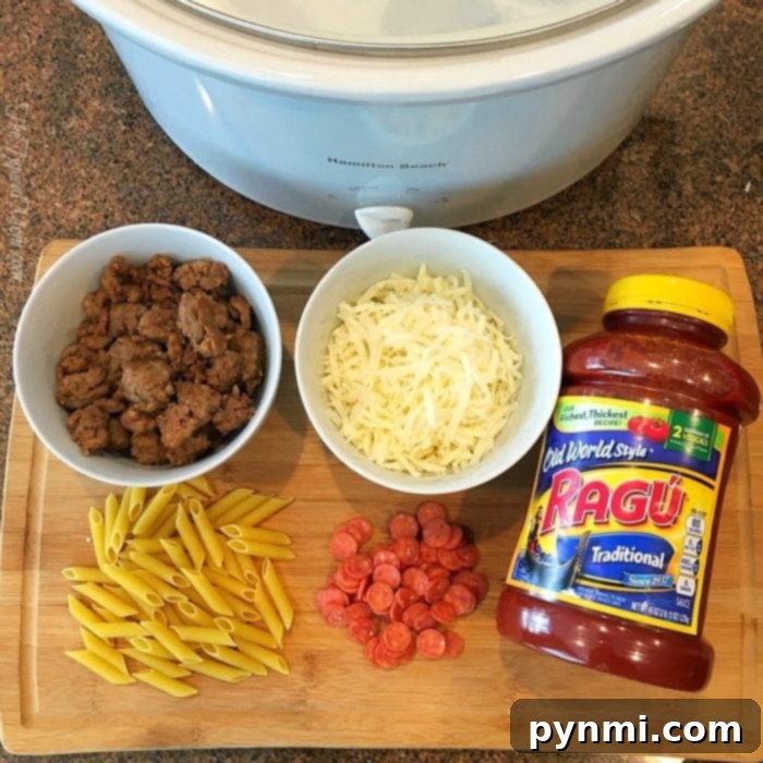 Ingredients for a hearty slow cooker pizza casserole are spread across the cutting board: uncooked penne, cooked sausage, shredded cheese, mini pepperoni, and a jar of Ragú sauce, all ready to be combined in the Hamilton Beach slow cooker.