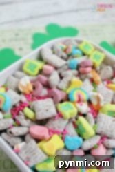 A colorful cereal mix with marshmallows, sprinkles, and square cereal pieces in a white bowl is reminiscent of a playful twist on a classic Peanut Butter Muddy Buddies recipe.