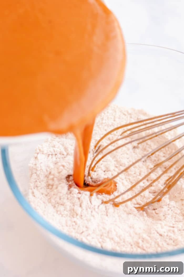 Golden Harvest Baked Pumpkin Donuts 4 Pumpkin puree being poured into a bowl of dry ingredients with a whisk, creating the perfect base for baked pumpkin donuts.