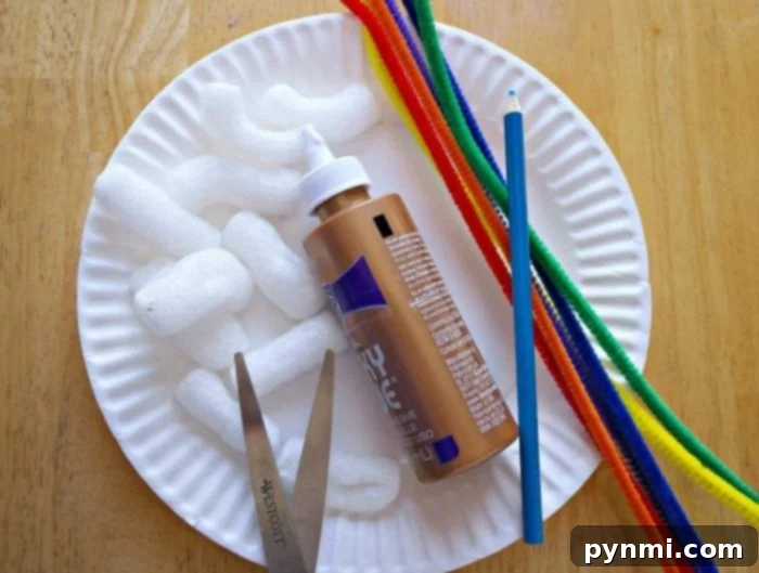 Kaleidoscope Weave Art 2 A paper plate holds packing peanuts, a bottle of brown craft glue, a pencil, colorful pipe cleaners ready for rainbow weaving art, and a pair of scissors on a wooden surface.
