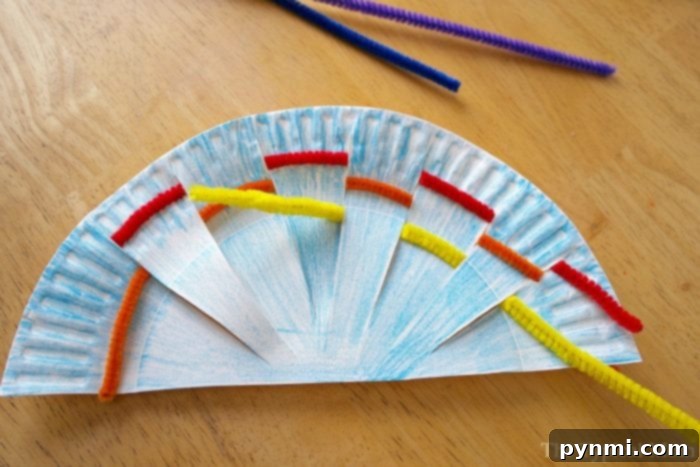 Kaleidoscope Weave Art 4 A paper plate decorated as a fan with rainbow weaving art using colorful pipe cleaners threaded through slits. The plate is colored in blue, and the pipe cleaners are red, yellow, and orange. The vibrant craft rests on a wooden table.