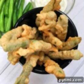 A bowl of perfectly crispy fried green beans served with a flavorful dipping sauce and a side of fresh green beans.