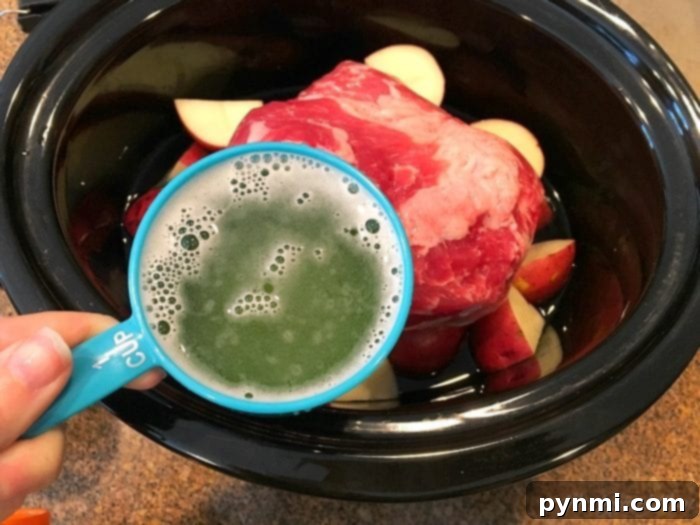 Slow cooker corned beef brisket is amazing! If you want to know how to cook corned beef brisket and cabbage in the crockpot it's super easy to do and should definitely be made more often than just on St. Patrick's Day. A person pours beer over a corned beef brisket in a slow cooker with potatoes, perfecting this succulent dish.