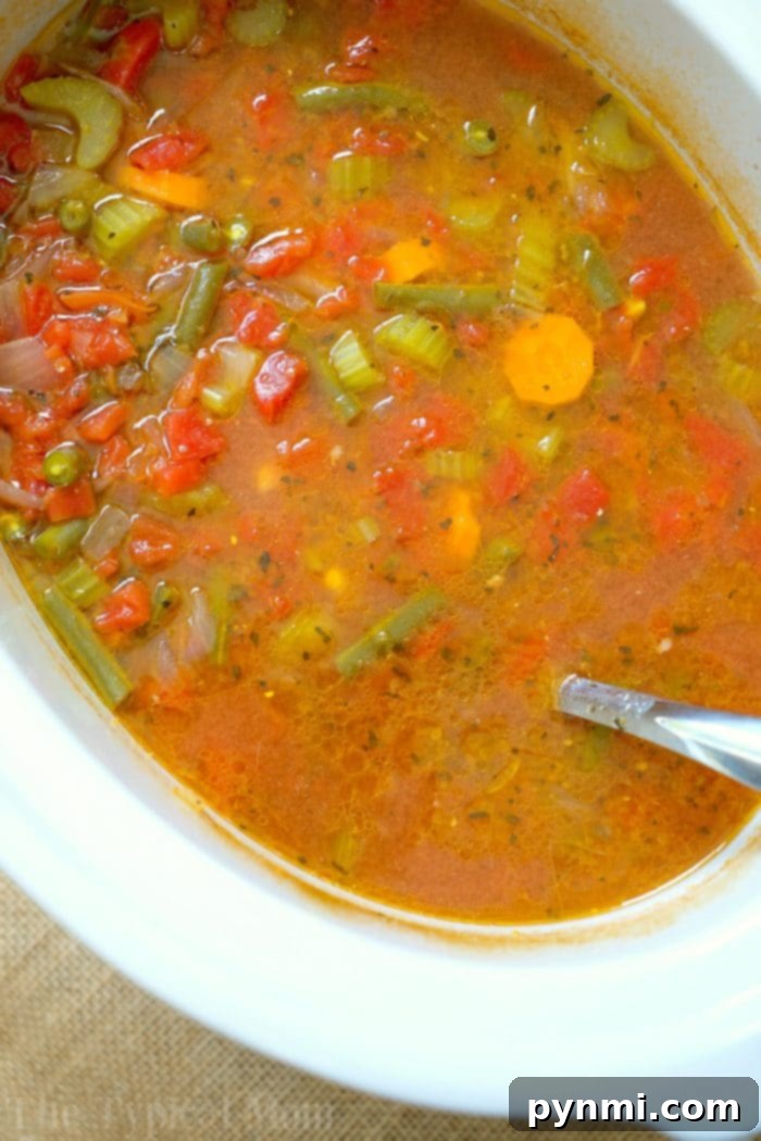 A large pot of hearty vegetable beef soup simmering gently in a slow cooker.