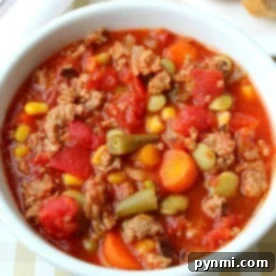 A crock pot full of hearty vegetable beef soup, brimming with corn, carrots, green beans, and tomatoes.