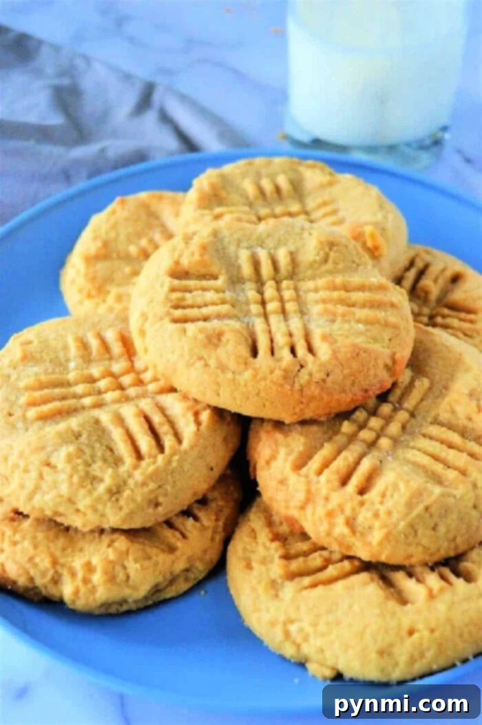 A plate of golden-brown peanut butter cookies, perfectly adorned with crisscross fork marks, sits invitingly next to a refreshing glass of milk.