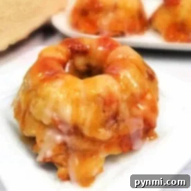 A Caramel Apple Bread Pudding mini bundt cake infused with the essence of caramel apple and finished with a luscious icing glaze, all elegantly displayed on a white plate.