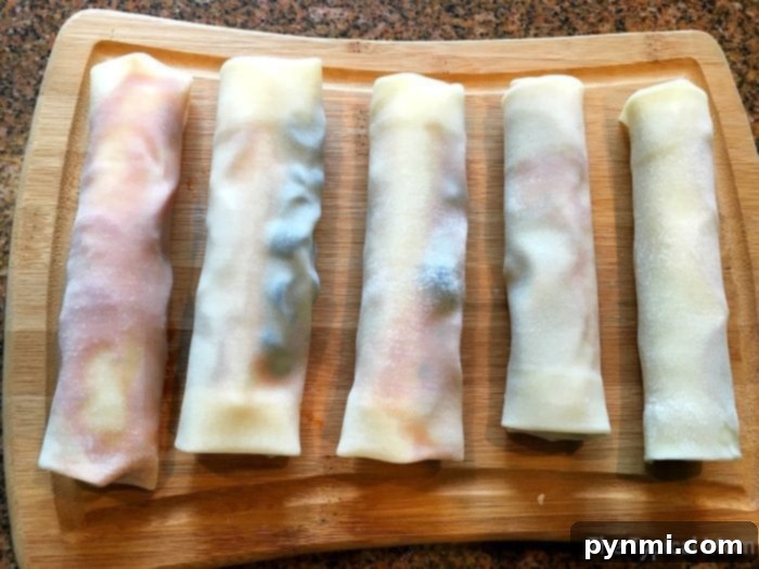 Pizzarolls 7 Several uncooked pizza egg rolls are neatly arranged on a wooden cutting board, showcasing their ready-to-fry state.