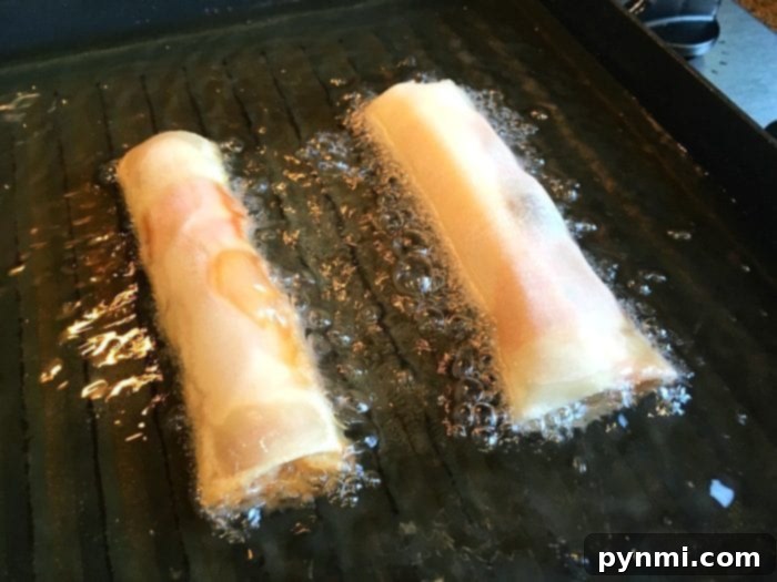 Pizzarolls 8 A close-up view of a hand carefully rolling a pizza egg roll wrapper with ingredients inside, demonstrating the preparation process.
