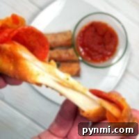 A hand stretches a cheesy pepperoni pizza roll with marinara sauce, surrounded by mouthwatering pizza egg rolls in the background.