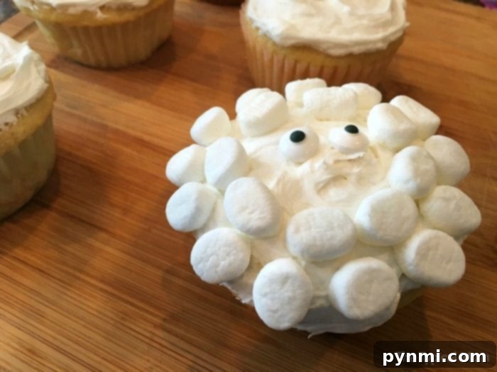 Finished sheep cupcakes, adorned with white frosting and mini marshmallows to perfectly mimic a sheep's face, rest charmingly on a wooden surface.