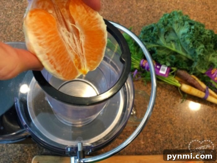 Unlock the Power of Kale: Juicing Made Easy 6 A hand squeezes an orange into a juicer, while kale and carrots sit in the background on a countertop, ready to inspire easy kale recipes.