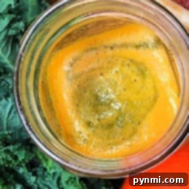 Top view of a glass of orange juice surrounded by fresh ingredients—kale, apples, carrots, and vibrant purple carrots—perfect for easy kale recipes.