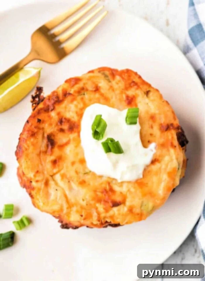 potato cake topped with sour cream and green onions on a white plate, alongside a lime wedge, fork, and an enticing dollop of fried mashed potatoes with cheese.