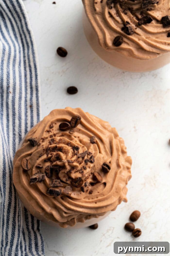 Whipped Coffee Delight 6 Two bowls of creamy chocolate coffee frosting, elegantly topped with cocoa nibs and coffee beans, resting on a white surface alongside a striped cloth