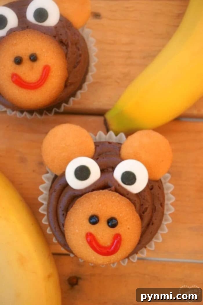 Close-up of three adorable monkey cupcakes with chocolate frosting, vanilla wafer ears, candy eyes, and a cheerful red smile, perfect for a child's birthday party or baby shower.