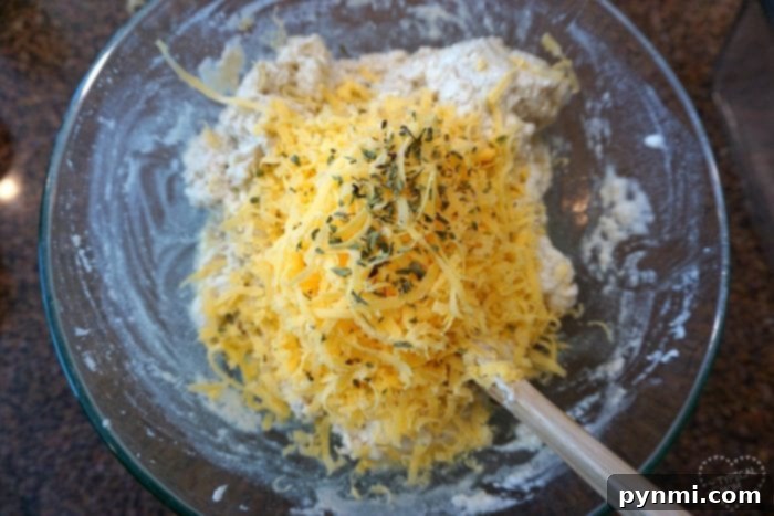 A glass bowl holds shredded cheese and fresh herbs, ready to be folded into the beer bread dough, emphasizing customization.