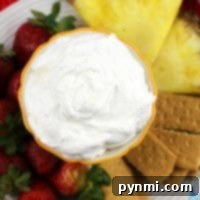 A bowl of creamy pina colada dip sits enticingly surrounded by sliced pineapple, strawberries, and graham crackers on a plate.