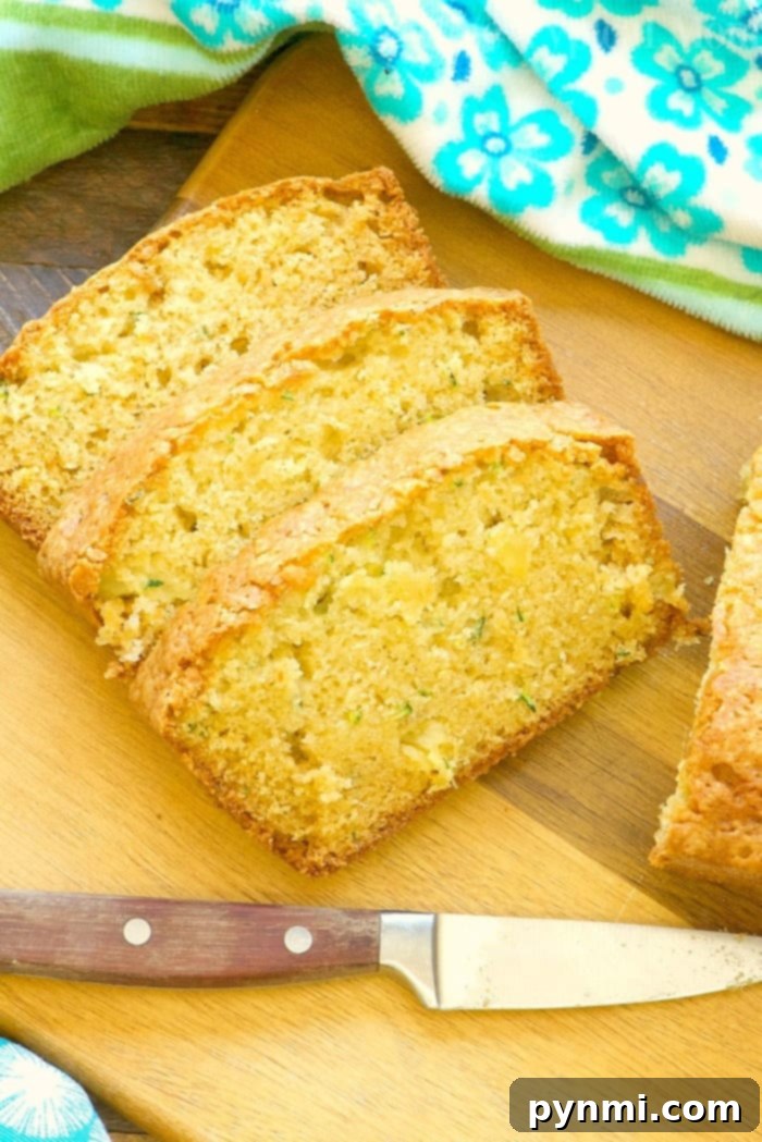Sliced zucchini pineapple bread on a wooden cutting board next to a knife with a dark handle, ready for serving.
