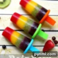 Three vibrant rainbow popsicles rest on a wooden surface, surrounded by an array of fresh fruit slices.